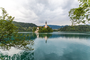Obraz premium Bled, Slovenia - July, 2019: Lake Bled with St. Marys Church of Assumption on small island. Mountains and valley on background. Space for your text.