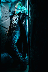 Fashion portrait of the young beautiful alternative man in leather long coat ready for party over silver and neon light studio background