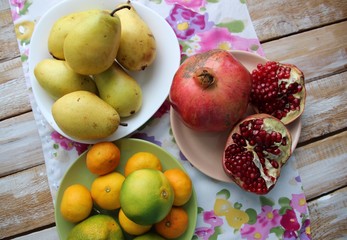 fresh fruits: pears, mandarins, pomegranate on colorful cover on wooden table