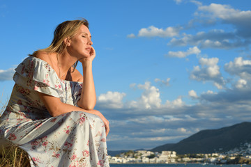 Woman sitting in front of a coastal landscape of the northern mediterranean on a summer afternoon with wind taking a sunbath with copy space