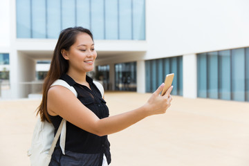 Smiling woman using mobile phone on street. Beautiful young female college student with backpack using cell phone outdoors. Technology concept