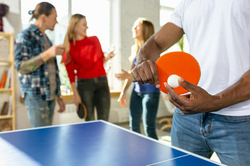 Young people playing table tennis in workplace, having fun. Friends in casual clothes play ping...