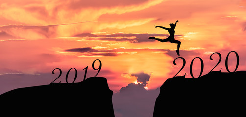 Happy new year 2020, Silhouette of 2020 letters on the mountain with business people jump across gap of mountain at sunrise.