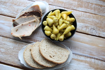 Green small hot pickled peppers in bowl with grain bread, ham, egg on wooden background