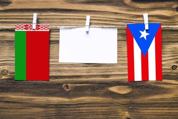 Hanging flags of Belarus and Puerto Rico attached to rope with clothes pins with copy space on white note paper on wooden background.Diplomatic relations between countries.