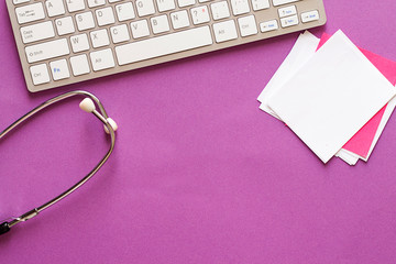 stethoscope, sticky note and keyboard on purple background