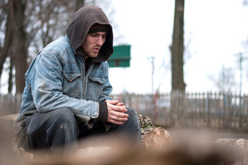 Homeless, sad man in a beanie sitting outside and feeling cold, trying to warm up his hands