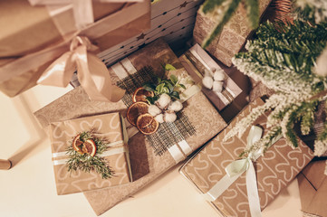 Christmas stylish eco gift boxes made with craft paper on floor near decorated fir tree branches. Christmas background with trendy gift box. Christmastime celebration. Festive holiday eve concept