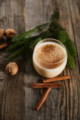 delicious eggnog cocktail near spruce branch, cinnamon sticks and walnuts on wooden table