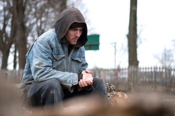 Homeless, sad man in a beanie sitting outside and feeling cold, trying to warm up his hands