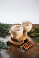 flavored eggnog cocktail on round boards, spruce branches, cinnamon sticks and walnuts isolated on grey