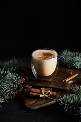Obraz na płótnie Canvas flavored eggnog cocktail on chopping board, cinnamon sticks and spruce branches isolated on black