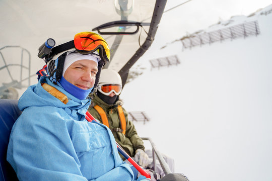 Image of two snowboarders in helmet and mask on cable car .