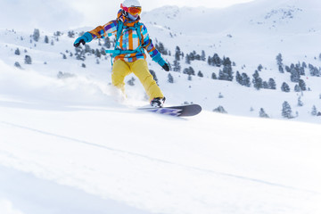 Athlete woman in helmet and mask is riding on snowboard on snowy slope at winter day.