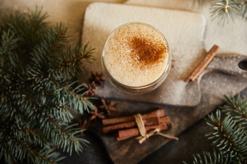 top view of flavored eggnog cocktail on cutting board covered with sugar powder, cinnamon sticks and spruce branches