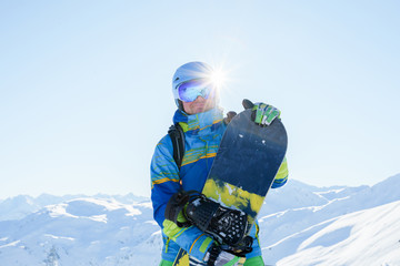 Image of sportsman in blue helmet and goggles with snowboard at ski resort in afternoon. - obrazy, fototapety, plakaty