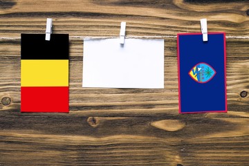 Hanging flags of Belgium and Guam attached to rope with clothes pins with copy space on white note paper on wooden background.Diplomatic relations between countries.