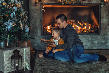 Dad plays with his son in the New Year at the Christmas tree and fireplace.