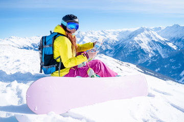 Fototapeta na wymiar Photo of snowboarder brunette woman in helmet with map in her hands sitting on mountain slope