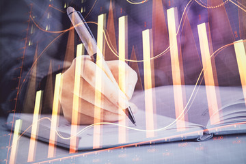 Double exposure of woman's hands making notes with forex graph hologram. Concept technical analysis.