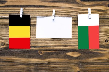 Hanging flags of Belgium and Madagascar attached to rope with clothes pins with copy space on white note paper on wooden background.Diplomatic relations between countries.