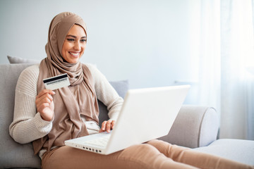 Arab woman making online purchase on laptop. Portrait of happy woman purchasing product via online...