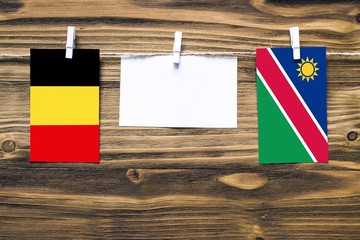 Hanging flags of Belgium and Namibia attached to rope with clothes pins with copy space on white note paper on wooden background.Diplomatic relations between countries.