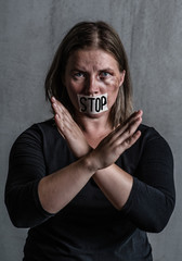 Beaten up woman victim of domestic violence and abuse with covered her mouth shows stop gesture