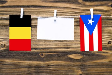 Hanging flags of Belgium and Puerto Rico attached to rope with clothes pins with copy space on white note paper on wooden background.Diplomatic relations between countries.