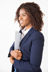 Happy joyful businesswoman holding folder with documents, looking away. Young African American...