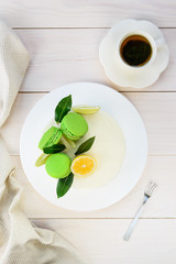 A homemade cake with a cream cheese, decorated by macarons, fresh lemon and lime on a white wooden table.
