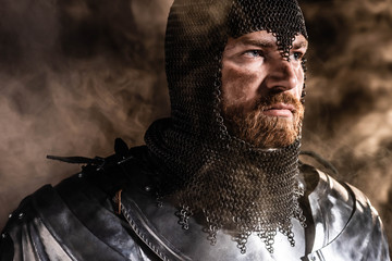 handsome knight in armor looking away on black background - obrazy, fototapety, plakaty