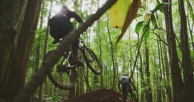 Extreme sports mountain bikers catch big air in slow motion, two friends mountain biking together in a green forest, fun outdoors summer activities