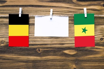 Hanging flags of Belgium and Senegal attached to rope with clothes pins with copy space on white note paper on wooden background.Diplomatic relations between countries.