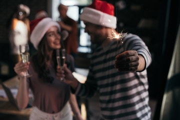 Fototapeta na wymiar selective focus of happy businessman and businesswoman in santa hats looking at each other while holding champagne glasses