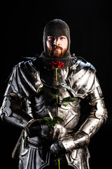 Naklejka premium handsome knight in armor holding rose isolated on black