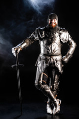 smiling knight in armor looking at camera and holding sword on black background