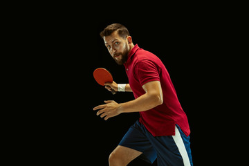 Young man plays table tennis on black studio background. Model in sportwear plays ping pong....