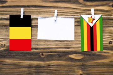 Hanging flags of Belgium and Zimbabwe attached to rope with clothes pins with copy space on white note paper on wooden background.Diplomatic relations between countries.