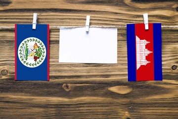 Hanging flags of Belize and Cambodia attached to rope with clothes pins with copy space on white note paper on wooden background.Diplomatic relations between countries.