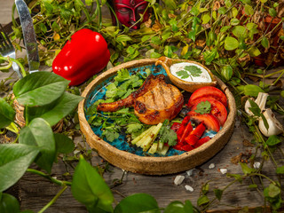Meat on the bone with vegetables in a craft plate. White sauce