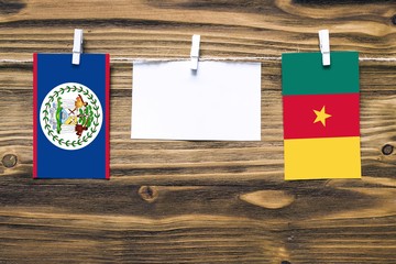 Hanging flags of Belize and Cameroon attached to rope with clothes pins with copy space on white note paper on wooden background.Diplomatic relations between countries.