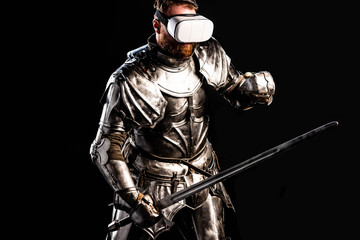 Naklejka premium knight with virtual reality headset in armor holding sword and fighting isolated on black