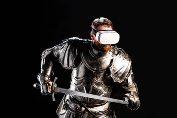 Naklejka premium knight with virtual reality headset in armor holding sword isolated on black