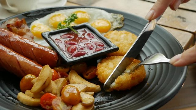 Woman eat traditional English breakfast with fried eggs, sausages, red beans, hash browns, mushrooms and tomatoes. Close-up