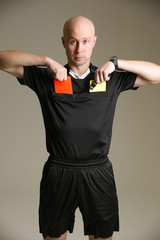 bald football referee on gray background. football referee pulls out a red and yellow cards from his pockets. football referee in a black uniform holding a red and yellow card