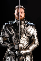 handsome knight in armor holding sword isolated on black