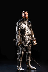 Fototapeta na wymiar handsome knight in armor holding sword isolated on black
