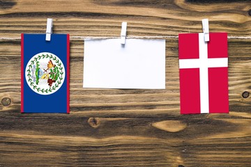 Hanging flags of Belize and Denmark attached to rope with clothes pins with copy space on white note paper on wooden background.Diplomatic relations between countries.