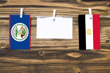 Hanging flags of Belize and Egypt attached to rope with clothes pins with copy space on white note paper on wooden background.Diplomatic relations between countries.